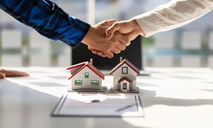 Apretón de manos sobre maquetas de casas y un contrato de arriendo