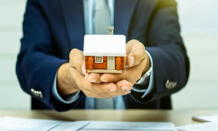 Persona de traje sosteniendo una casa en miniatura entre las manos